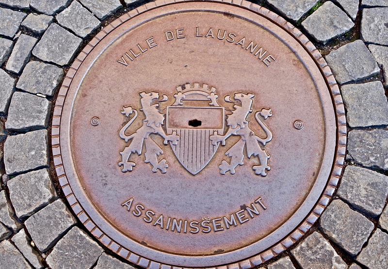 capital letter, cover, maintenance-hole, sewer, close-up, circular, lid, circle, geometric shape, communication, metal, directly above, city, symbol, paving stone