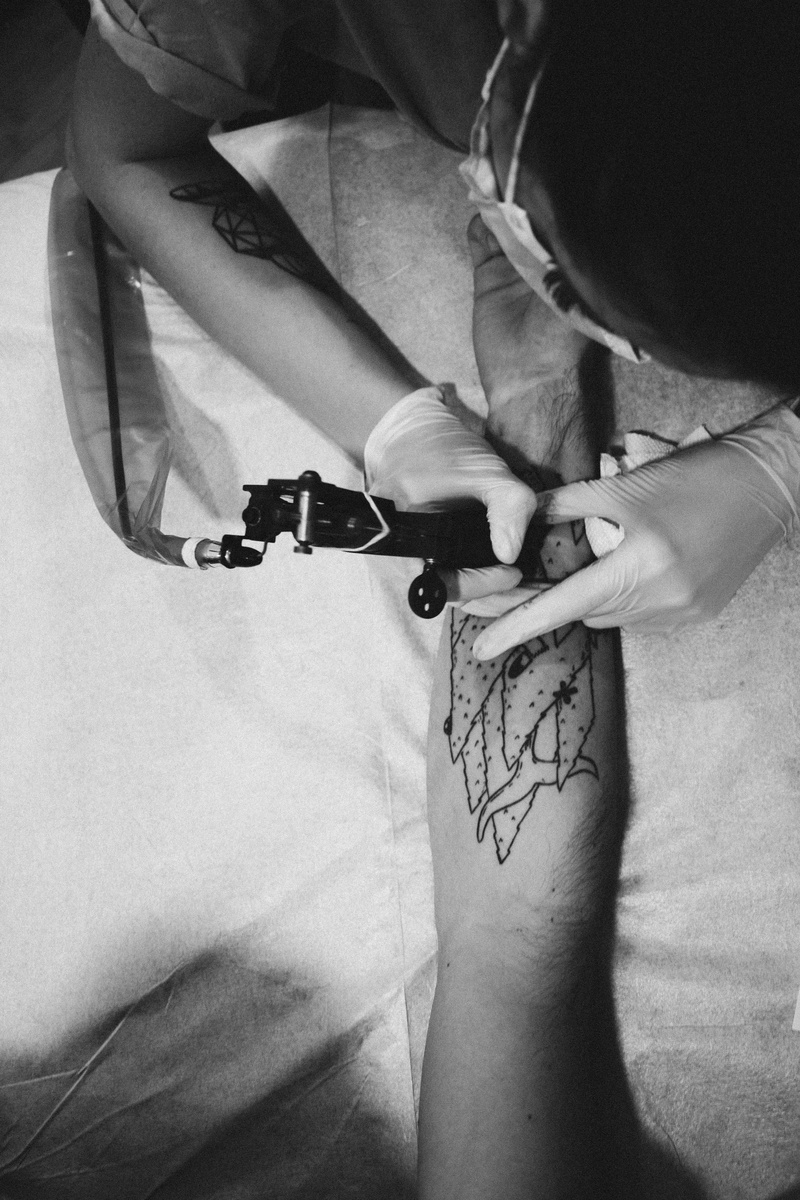 sitting, drawing, man, skill, aiming, black and white, accuracy, lifestyles, gun, leisure activity, creativity, hand, tattooing, machine, weapon, high angle view