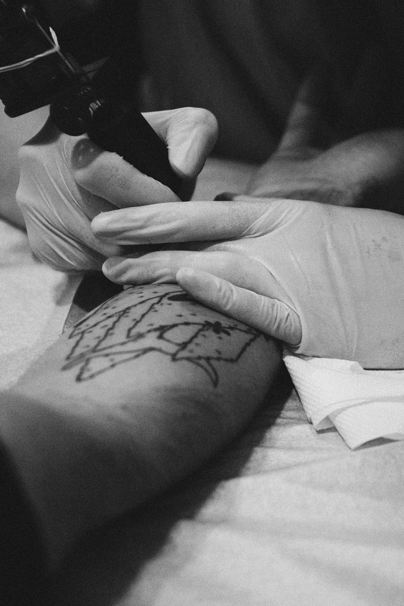 human limb, furniture, human finger, modern, human hand, tattoo shop, pain, 5K, tattoo studio, gloves, work, real people, indoors, tattoo artist, unrecognizable person