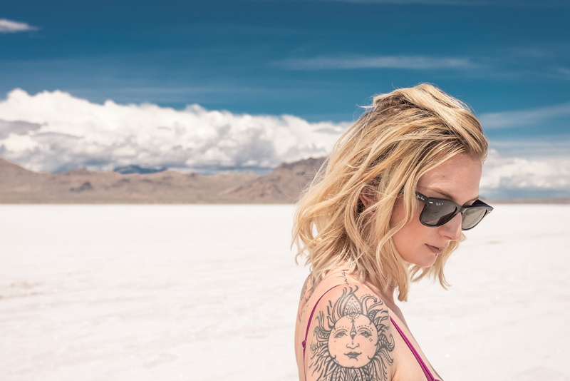 headshot, outdoors, black, day, wind, glasses, desert, one person, blond hair, looking down, short hair, land, person, nature, sunglasses, young women