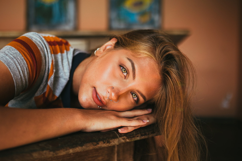 person, bright eyes, contemplation, beauty, depth of field, lying down, piercings, hairstyle, selective focus, photo, close, focus on foreground, indoors