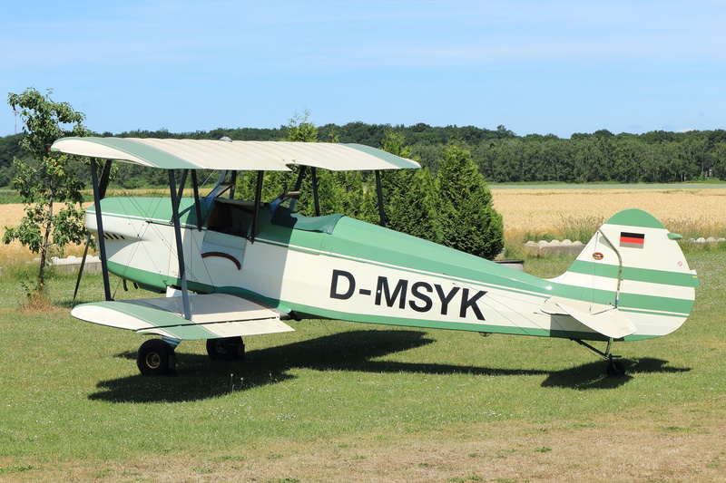air vehicle, outdoors, green color, nature, road, propeller plane, oldtimer, sunny, blue, landscape, day, transportation, text, 5K, sunlight, plant, western script
