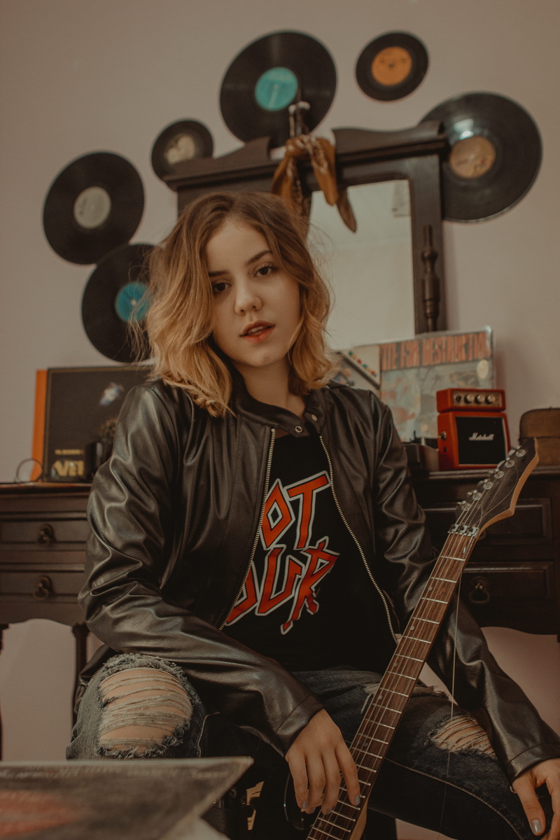 hair, leather jacket, home interior, woman, sitting, musical instrument, hairstyle, innocence, real people, chair, casual clothing, holding, human, guitar