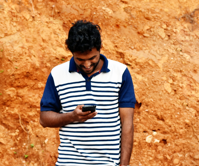 smart phone, telephone, smiles, style, outdoors, mobile phone, candid, holding, positive, real people, wall, poster, casual clothing, modal, emotions, tshirt