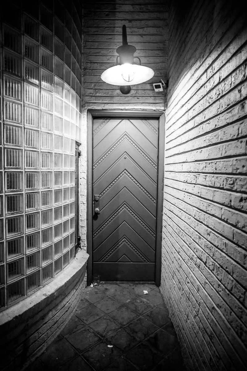 monochrome, door, built structure, light, black-and-white, security, indoors, building, electric lamp, illuminated, hallway, closed, electric light, wall