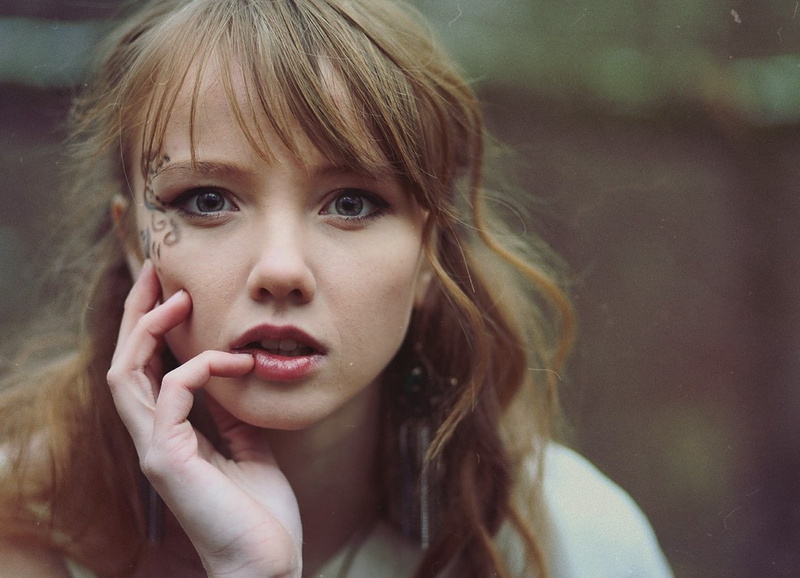 hairstyle, long hair, headshot, blue eyes, young adult, looking at viewer, contemplation, beautiful woman, front view, one person, tattoo, hair, blond hair