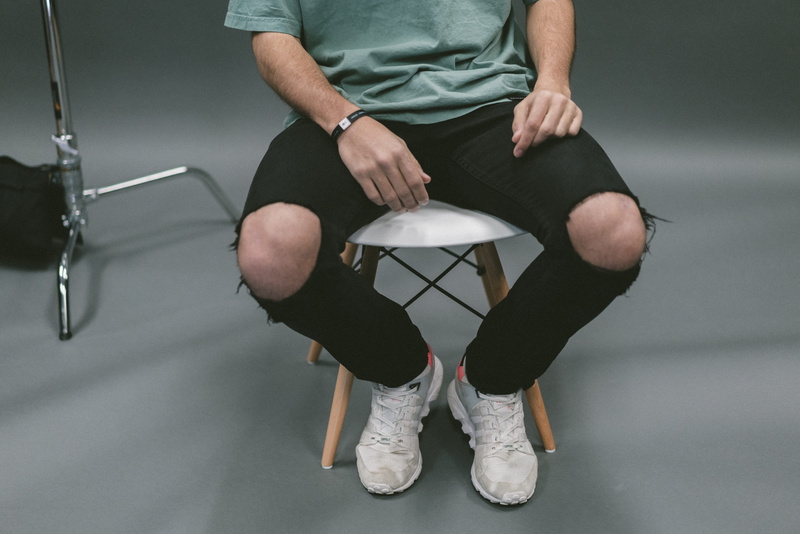 human leg, sitting, footwear, real people, shoe, people, seat, indoors, minimalist, lifestyles, gray background, low section, white, man, one person, midsection