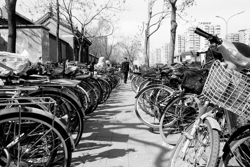 bicycle, built structure, mode of transportation, path, machine, pavement, tree, apparel, wheel, vehicle, town, walkway, outdoors, sidewalk, day, person