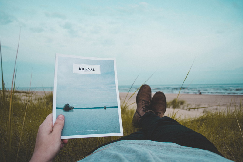 magazine, holding, shoe, human body part, sea, read, personal perspective, sand, black, journal, relaxation, outdoors, beach, land, reading, men, male