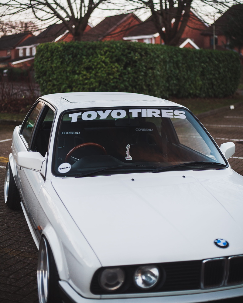 sedan, bmw, mode of transportation, light, machine, parking, outdoors, tire, windshield, no people, motor vehicle, street, land vehicle, focus on foreground