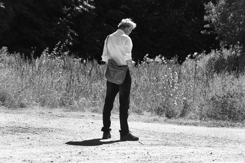 day, sunny day, full length, alone, sunlight, real people, outdoors, solitary, plant, white shirt, footpath, people, checking phone, young adult, editorial