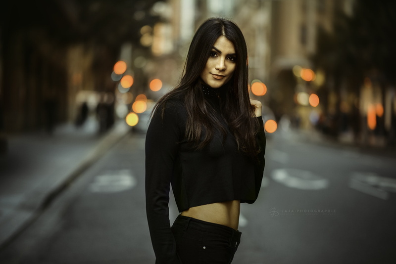 brunette, front view, looking at viewer, focus on foreground, city life, depth of field, hair, city, standing, lifestyles, young women, black clothing