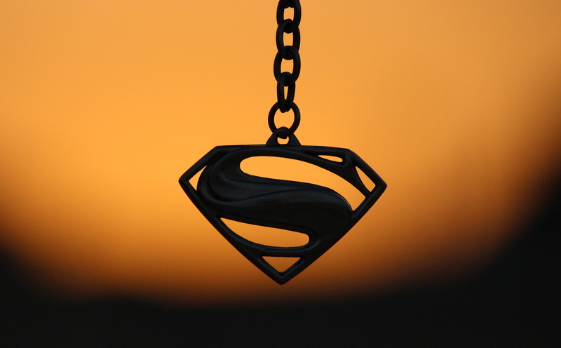 logo, indoors, single object, focus on foreground, jewelry, chain, Macro, fashion, superman, keychain, studio shot, still life, #hero, close-up, hanging