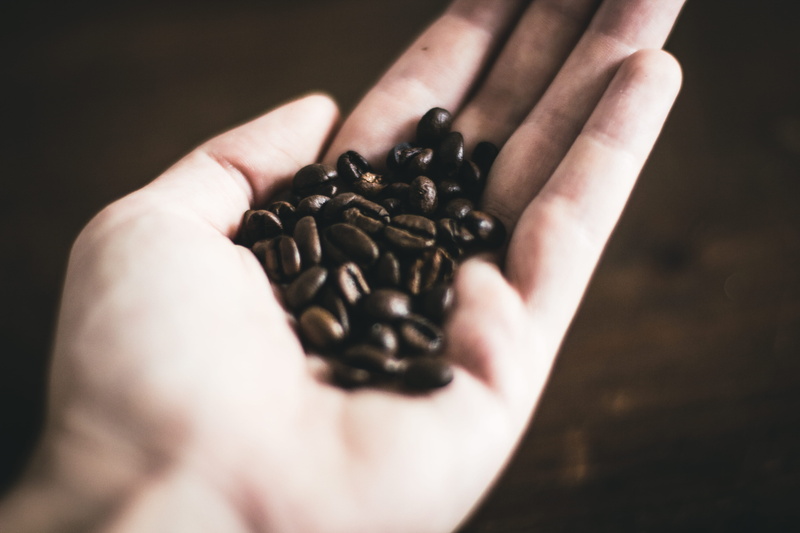 holding, food, people, caffeine, food and drink, table, real people, one person, coffee - drink, dark wood, cologne, finger, brown, freshness, coffee bean