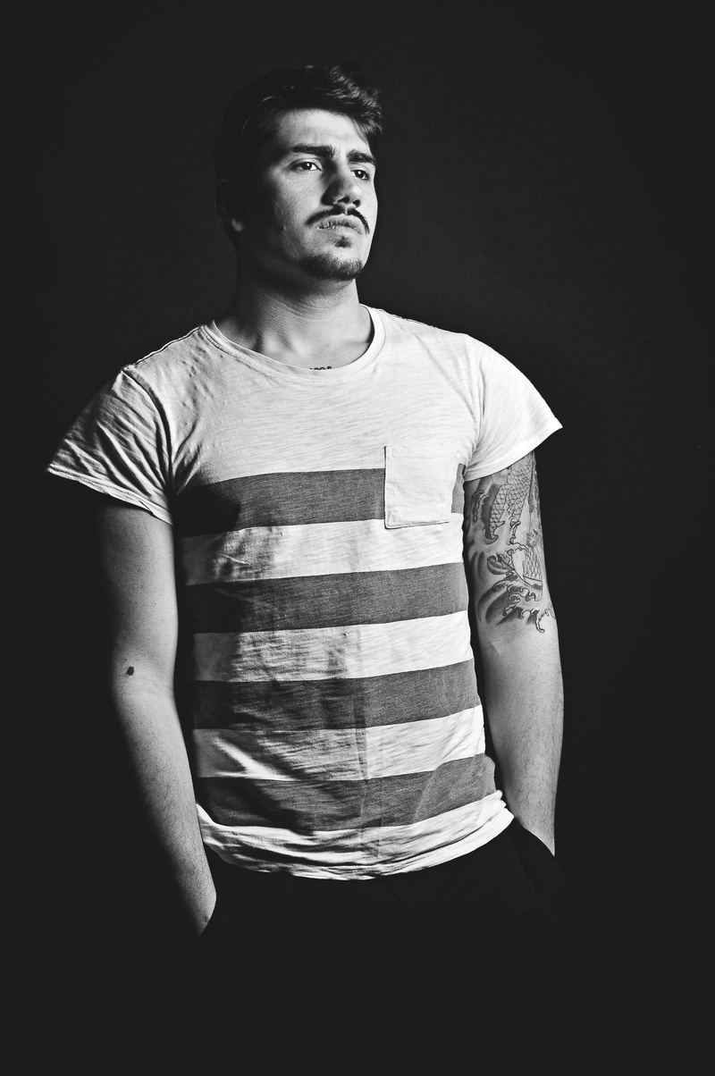 grayscale, young men, looking at camera, light, standing, black and white, one person, indoors, skin, face, tattoo, model, black background, front view