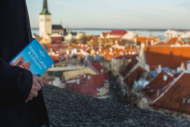 travel, book, standing, roof, baltic, focus on foreground, outdoor, residential district, shadow, sunlight, guidebook, building exterior, cityscape, crowded