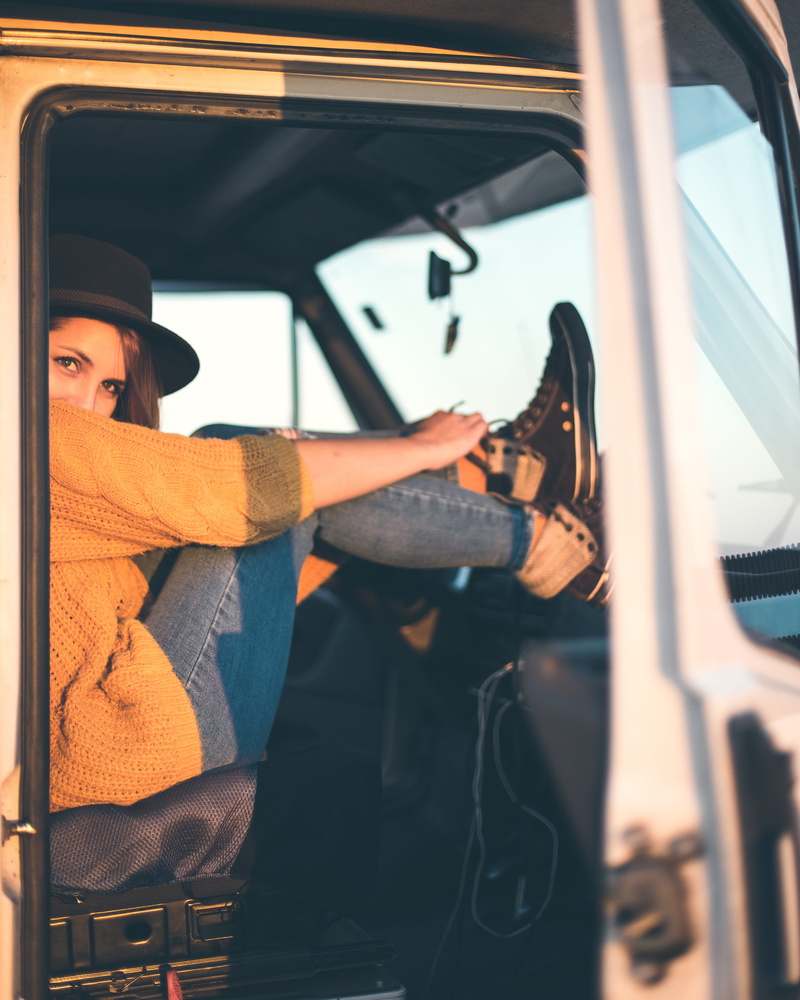 shoe, one person, window, vanlife, lifestyles, land vehicle, boot, person, woman, footwear, real people, sitting, holding, mode of transportation, car