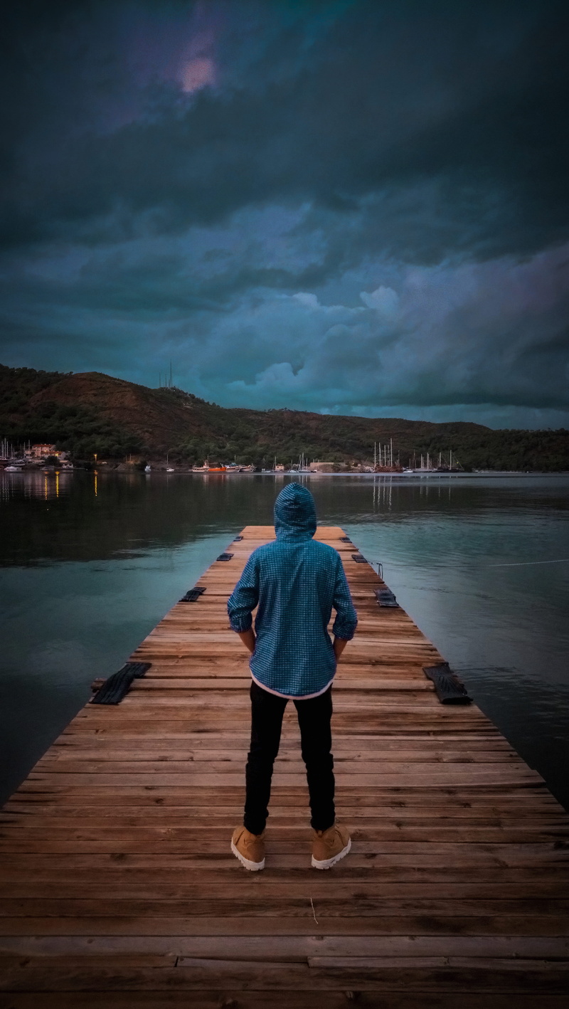 leisure activity, sea, nature, hoodie, leisure, one person, river, wearing, recreation, wooden, looking at view, tranquil scene, cloud - sky, full length