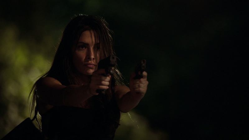 black background, headshot, Sarah Shahi, looking at camera, one person, night, adult, women, front view, portrait, holding, weapon, dark, emotion, sign