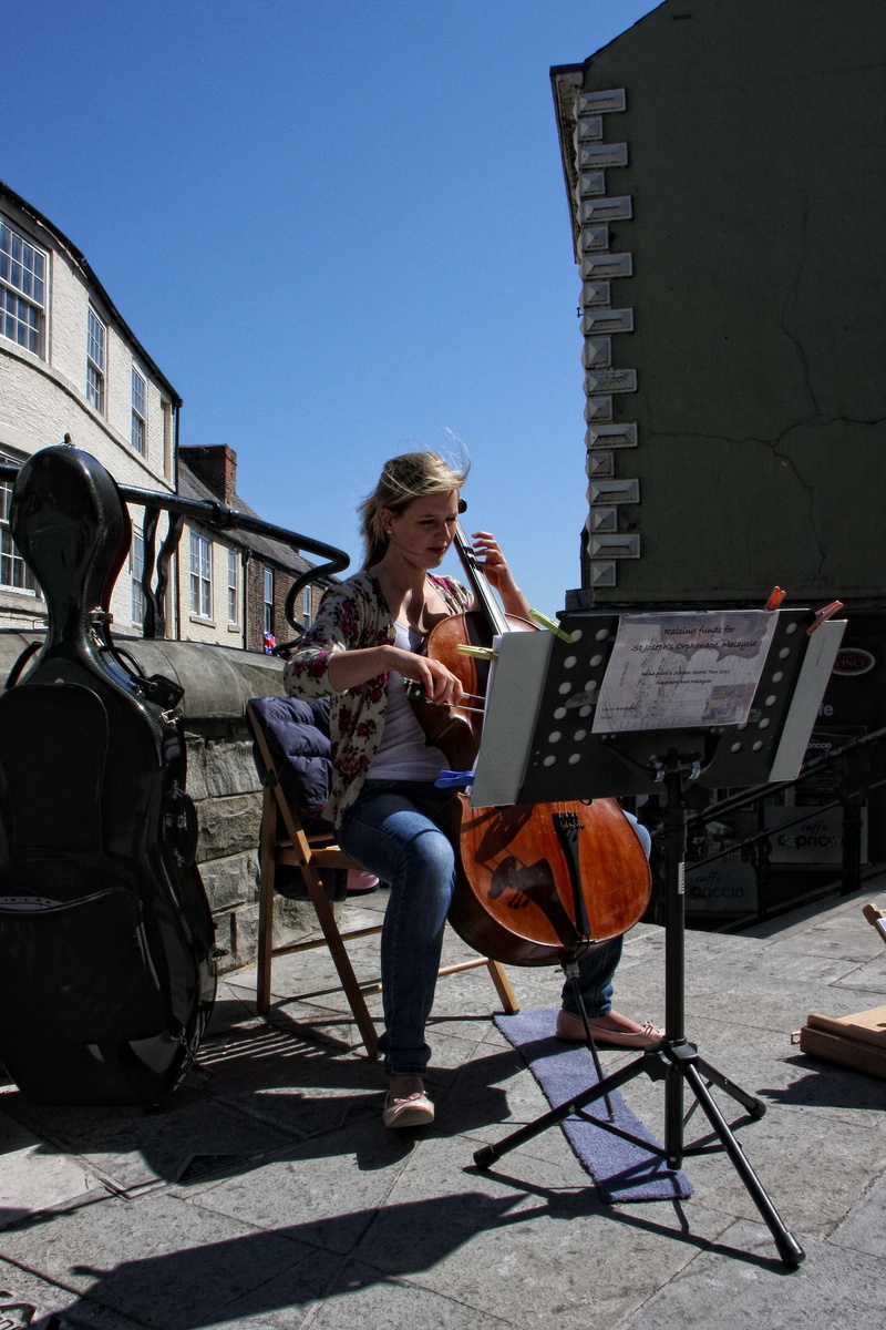full length, sunlight, clear sky, sitting, building exterior, music, girl, sky, entertainer, built structure, busker, lifestyles, shadow, real people, hairstyle
