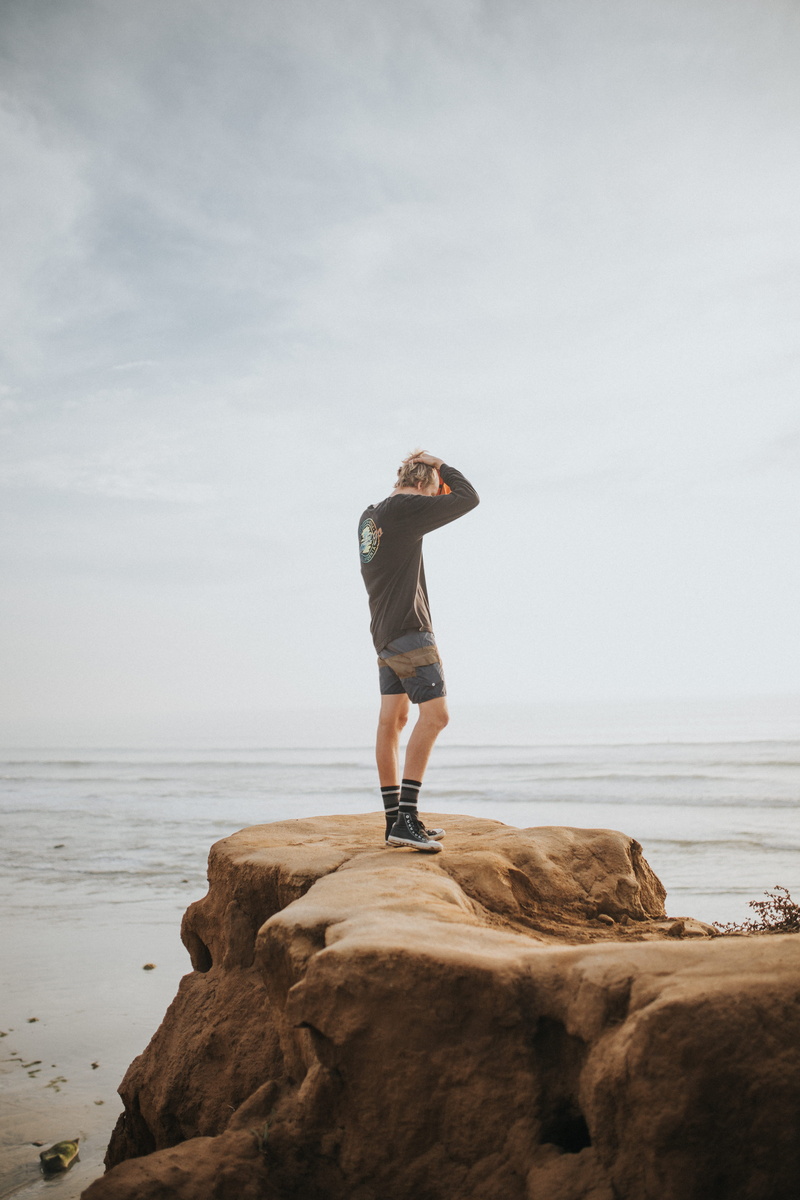 ocean, coast, footwear, standing, formation, daytime, shorts, rock - object, terramar cliffs, casual clothing, solid, shoreline, sea, beauty in nature