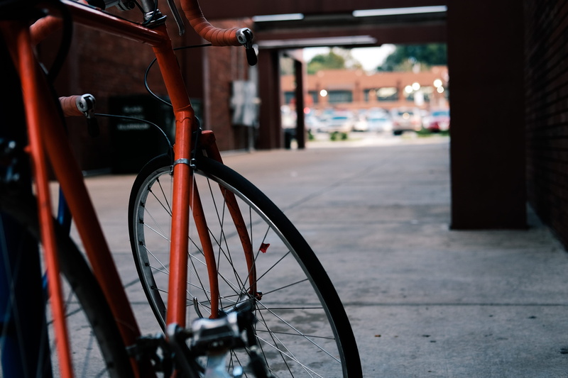 red, built structure, sidewalk, wheel, wall, mode of transportation, black, day, gray, architecture, outdoors, road, stationary, beside, tire, footpath