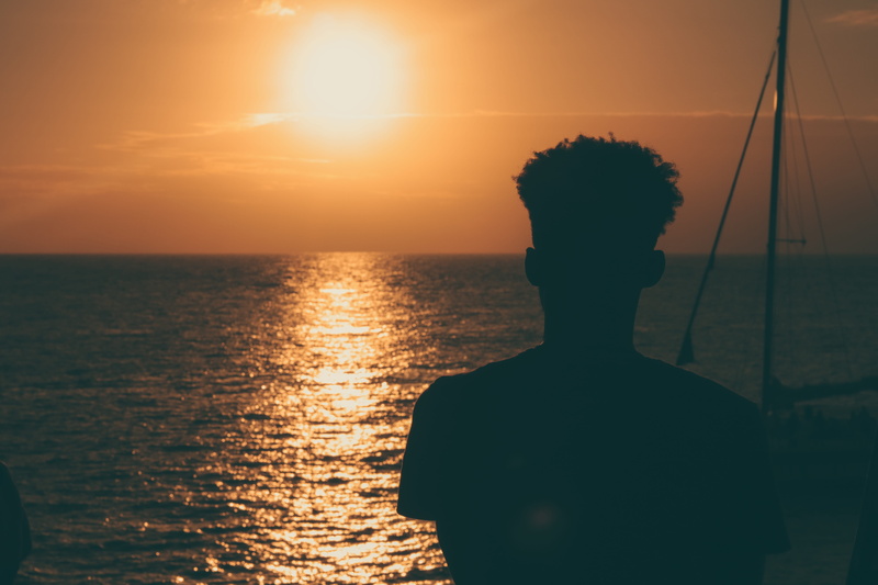 scenics - nature, sky, real people, water, man, tranquility, silhouette, contrast, looking at view, boat, leisure activity, sun, beach, horizon over water