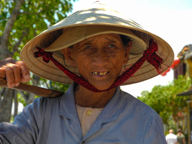headshot, lady street vendor, hue, human body part, asian style conical hat, men, body part, clothing, obscured face, focus on foreground, day, adult, outdoors