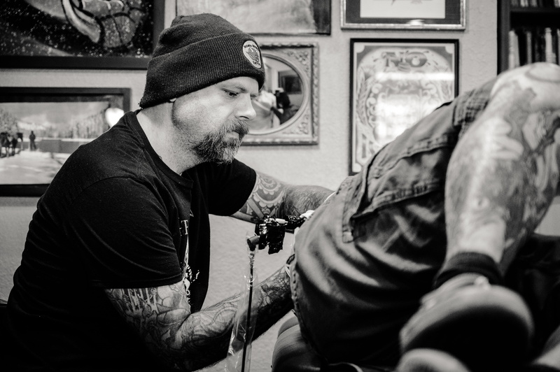 mid adult, one person, cap, another, lifestyles, clothing, person, sit, artist, adult, day, tattoo artist, real people, beanie, recreation, black-and-white