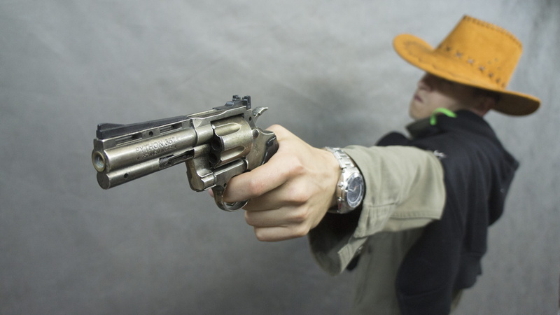 sombrero, focus on foreground, weapon, cowboy hat, weaponry, gray, mid adult, studio shot, gun, wristwatch, standing, metal, clothing, holding, apparel
