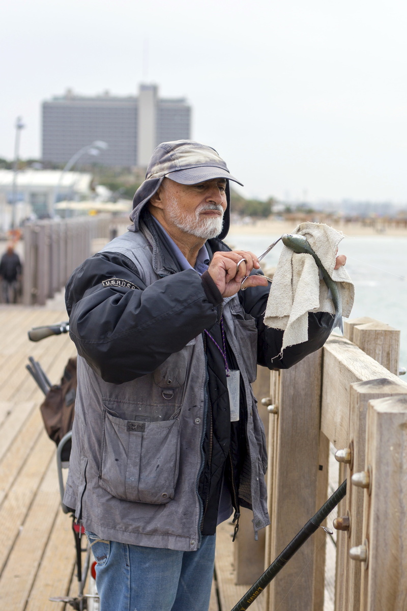 focus on foreground, one person, fisherman, holding, day, standing, technology, fish, street, water, clothing, senior men, man, side view, sea, architecture