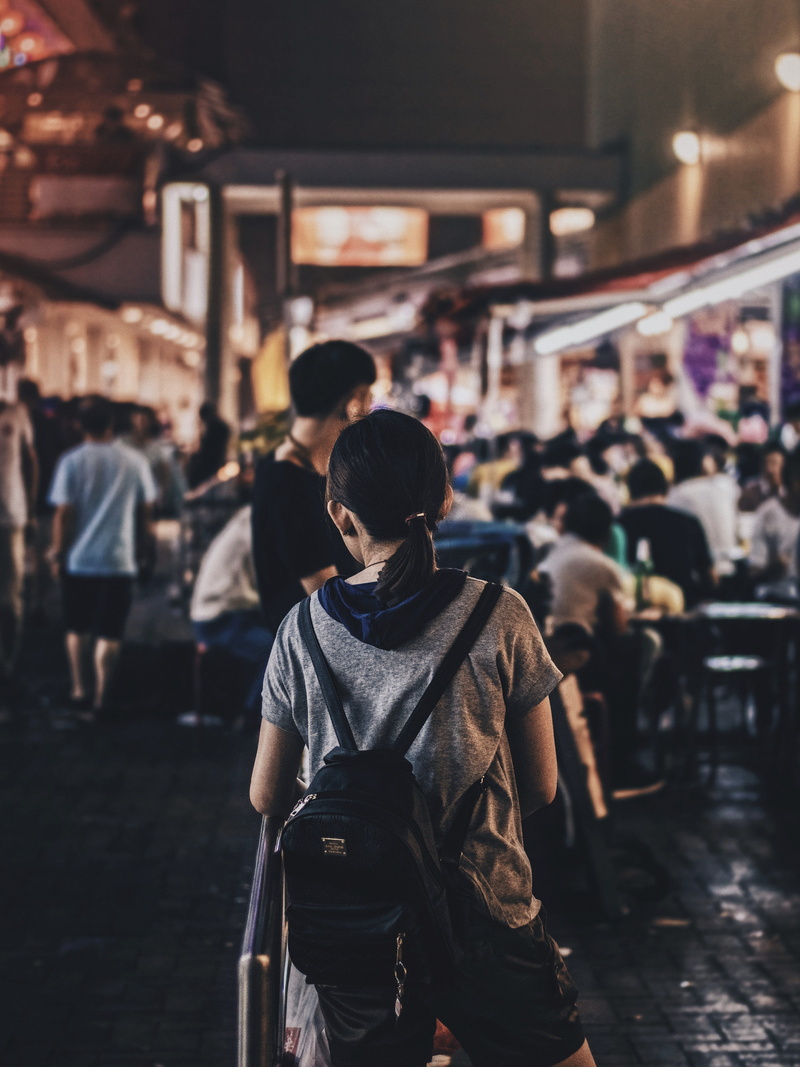 three quarter length, standing, city, architecture, alleyway, girl, focus on foreground, building, incidental people, crowd, backpack, kiss, built structure