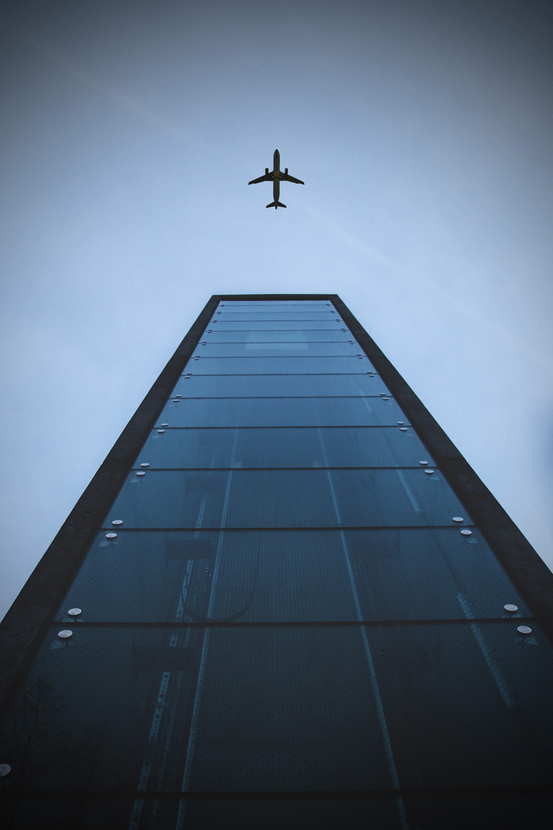 directly below, architecture, building exterior, day, no people, air vehicle, clear sky, wings, built structure, buiding, mid-air, shot, mode of transportation