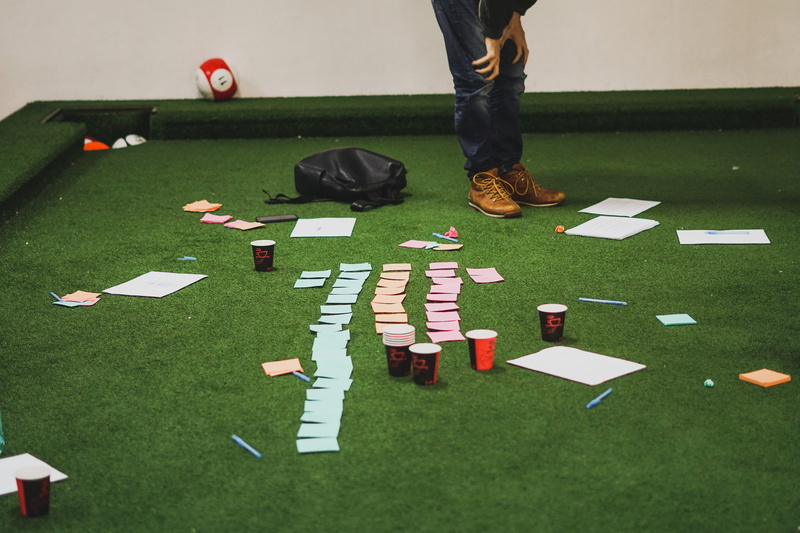 plant, outdoors, workshop, postit, teambuilding, notes, person, flooring, high angle view, table, cups, men, human, apparel, game, leisure games, leisure activities