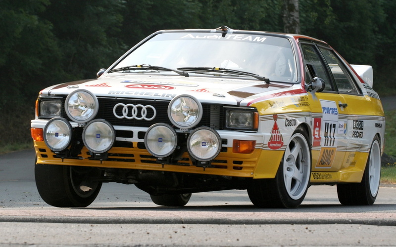 Group B, Rally car, land vehicle, no people, vintage car, coupe, city, transportation, metal, outdoors, car, background, street, the front, public transportation
