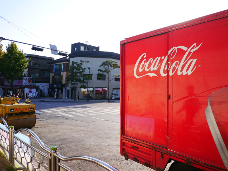 outdoors, Tea, land vehicle, built structure, no people, western script, day, clear sky, mode of transportation, sign, transportation, Coca Cola, architecture
