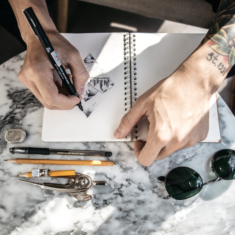 art supplies, sunglasses, sketching, human limb, 2K, real people, pens, business, holding, table, working, occupation, high angle view, thecoffee, human hand