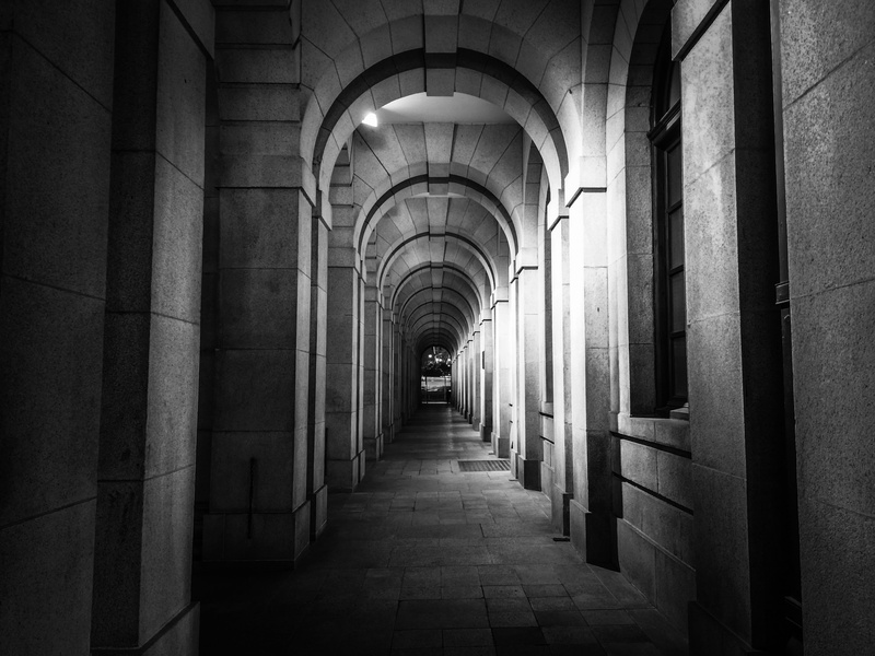illuminated, building, empty, arch, built structure, colonnade, statue square, no people, ceiling, direction, indoors, architecture, arcade, in a row, black and white