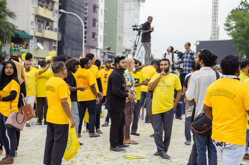 focus, large group of people, group, gathering, city, standing, group of people, city street, buildings, yellow, posters, outfit, man, yellow shirts, day