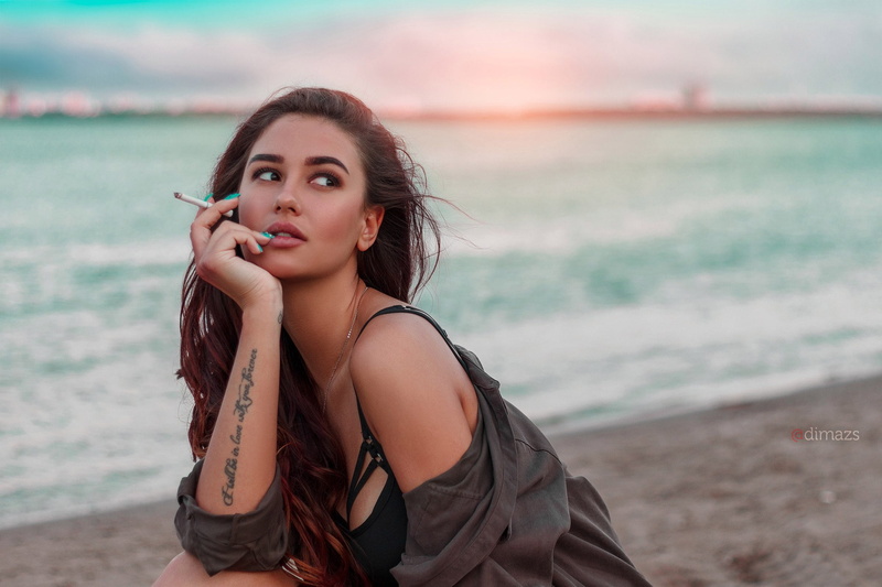 one person, outdoors, hair, focus on foreground, adult, looking at camera, black bras, beautiful woman, long hair, cigarettes, face, sea, fashion, smoking
