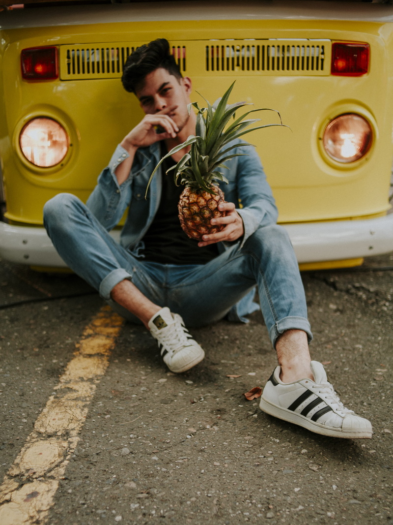 holding, footwear, yellow, adidas, transportation, leisure activity, young men, jeans, shoe, one person, young adult, human, mode of transportation, food