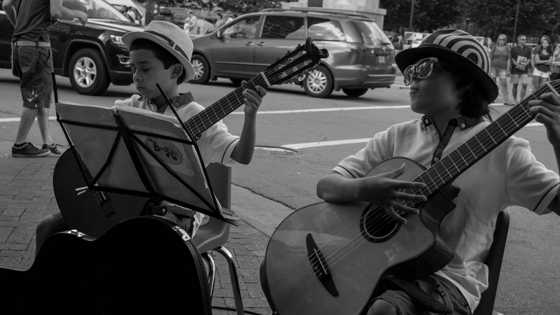 guitar, sunglasses, string instrument, musician, land vehicle, sidewalk, sitting, arts culture and entertainment, talent, musical equipment, black and white