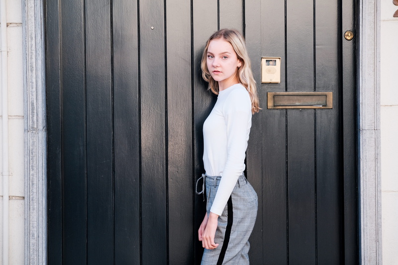 adult, door, lady, three quarter length, black, outdoors, person, girl, day, wall, front view, young, beside, casual clothing, young women, looking at camera
