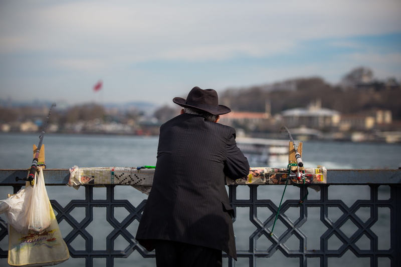 handrail, day, real people, bridge, transportation, outdoors, body, buildings, person, hat, railing, fish, coat, lifestyles, waterfront, apparel, sun hat