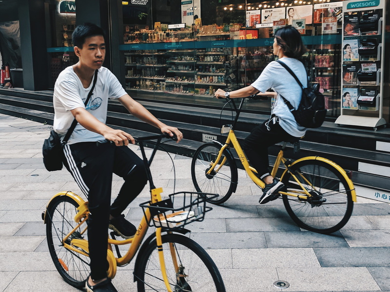 2K, riding, building exterior, land vehicle, casual clothing, store, lifestyles, asia, streetscape, pavement, chinese, full length, sitting, yellow, cycling