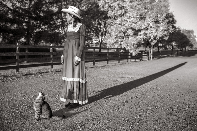 person, white, lazy, wearing, sitting, day, tree, canine, fence, park, one animal, black, hat, dog, and, ranch, outdoors, mammal, domestic, farm, acreage