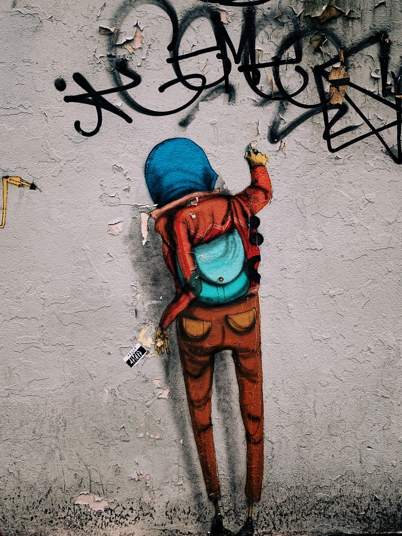 overcoat, mural, standing, wall - building feature, hooded, real people, asphalt, bike, transportation, apparel, tarmac, person, drawing, art, day, coat