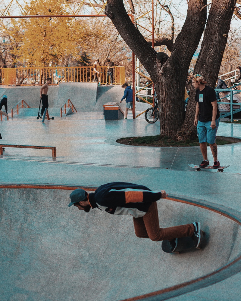 daytime, clothing, transportation, incidental people, bare tree, shoe, architecture, human, real people, city, sports, tree, trunk, skateboard park, amusement park