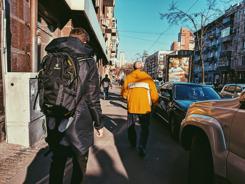 vehicle, day, person, raincoat, architecture, rear view, uniform, street, people, clothing, road, real people, coat, 2K, land vehicle, city, overcoat