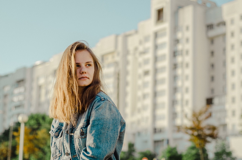architecture, urban, focus on foreground, female, front, built structure, jacket, brown hair, contemplation, standing, looking away, blue, human, portrait